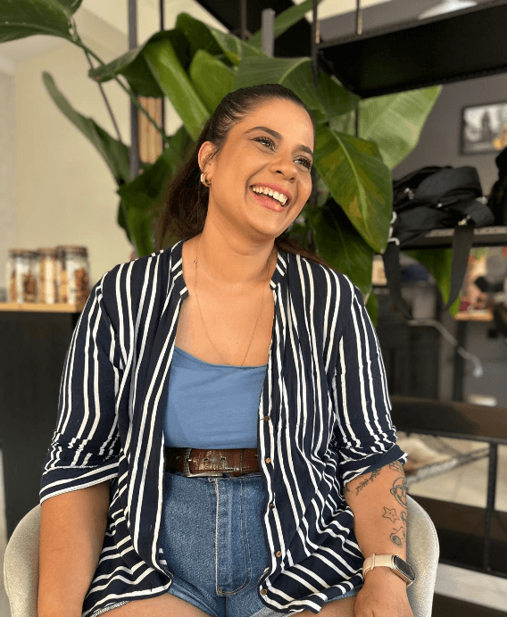 Fah Salviano sorrindo, sentada em um espaço com plantas ao fundo